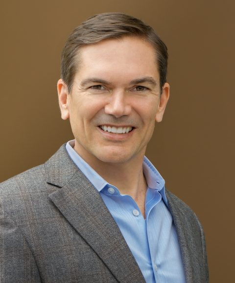 Tom O'Connor, founder of Action Plan Partners, in a grey jacket and open-collar blue shirt